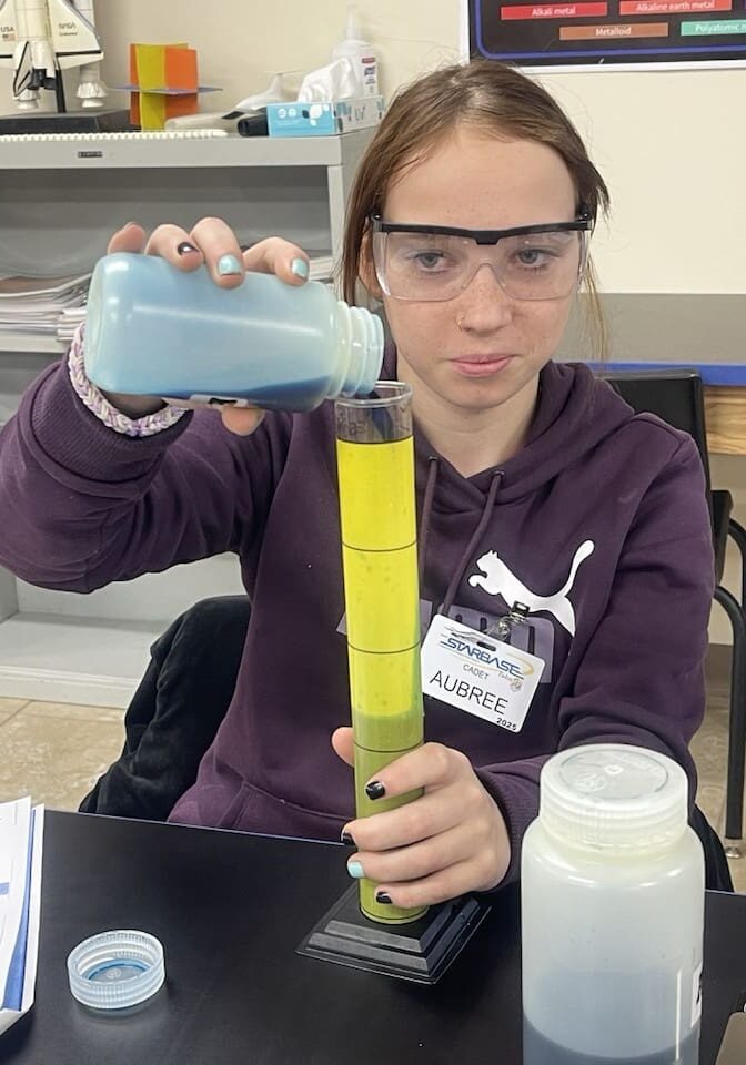 Student pouring liquid into a tall graduated cylinder.